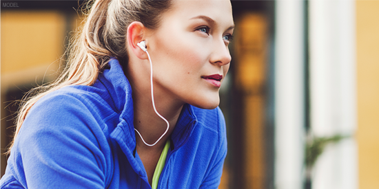Woman in blue jacket sitting and listening to music through apple headphones