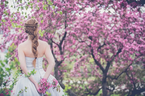 Woman in white dress standing in a field of trees with pink leaves