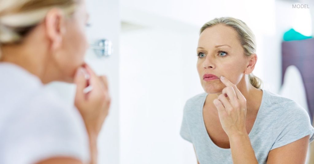 Woman with clear skin (model) carefully examining her face in the bathroom mirror.