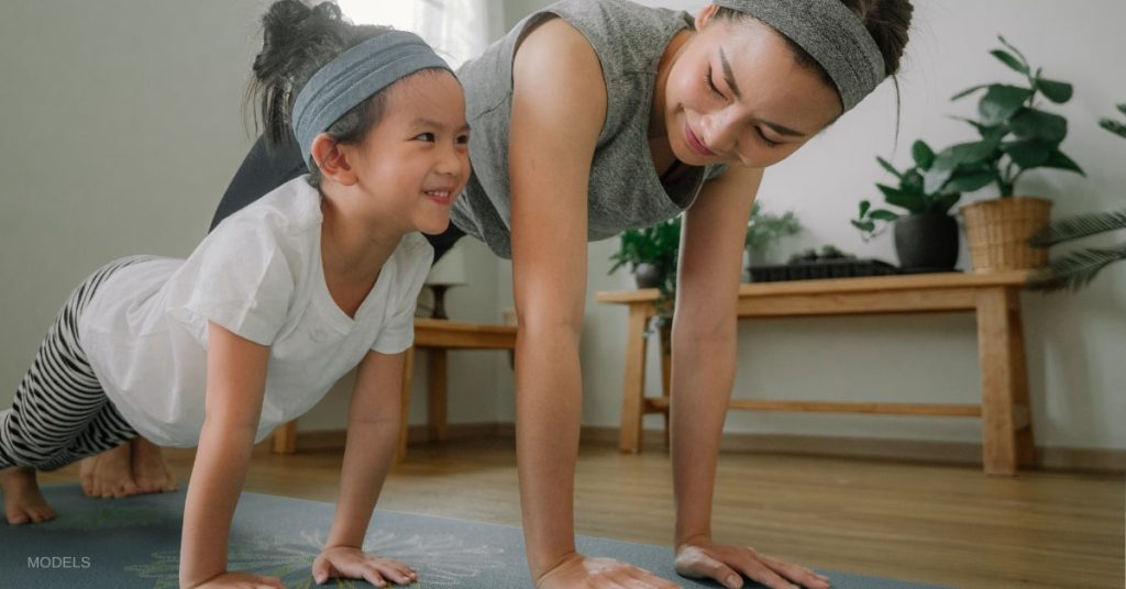 Woman and daughter (models) doing yoga in the living room.