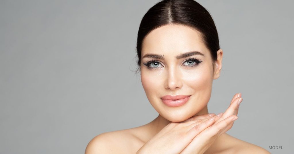 woman in mid 20s (model) with smooth skin looks into the camera against a gray background